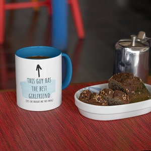 Pode incluir: Caneca de caf&eacute; branca com borda e al&ccedil;a azuis. A caneca tem um design de aquarela azul e branco com o texto "Este cara tem a melhor namorada (Sim, ela me comprou esta caneca)" e uma seta apontando para cima.