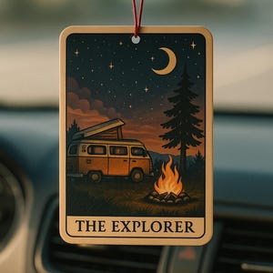 May include: Rectangular car air freshener with a camping scene. The design features a yellow van, a campfire, a crescent moon, and stars against a dark blue sky. The text "THE EXPLORER" is at the bottom. The air freshener hangs from a red string.