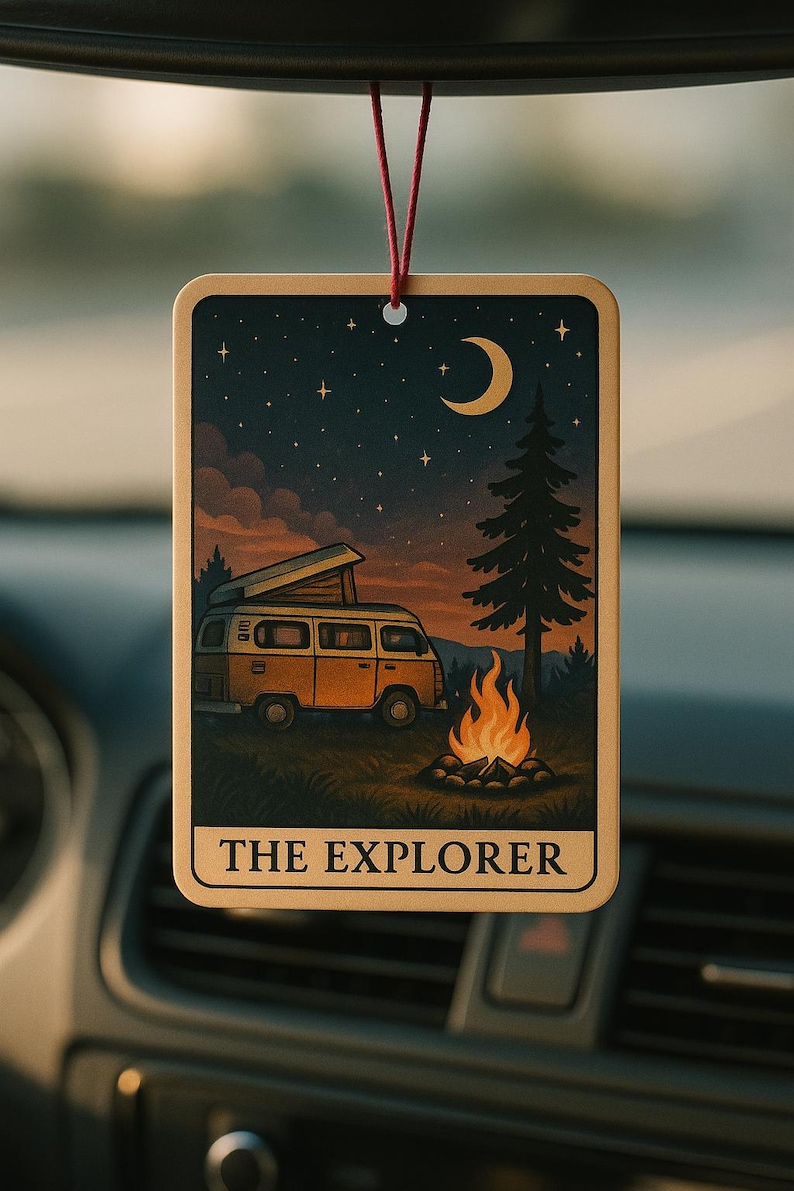 May include: Rectangular car air freshener with a camping scene. The design features a yellow van, a campfire, a crescent moon, and stars against a dark blue sky. The text "THE EXPLORER" is at the bottom. The air freshener hangs from a red string.