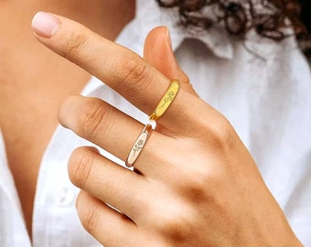 Puede incluir: Dos anillos, uno dorado y otro de oro rosa, se muestran en el dedo de una persona. Cada anillo presenta un delicado diseño floral. Los anillos son bandas simples con una cara rectangular, que muestra la flor grabada.