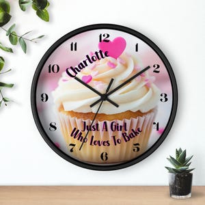 May include: A black and white clock with a cupcake design. The cupcake is white with pink frosting and sprinkles. The clock face has black numbers and hands. The text "Charlotte Just A Girl Who Loves To Bake" is printed on the clock face.