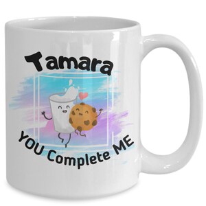 May include: White ceramic mug with a watercolor background and a cartoon milk carton and cookie holding hands. The text "Tamara You Complete Me" is printed on the mug.