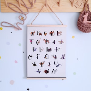 May include: A white poster with a black alphabet printed on it. Each letter is paired with an animal illustration. The poster is hanging on a wooden wall with a rope hanger.