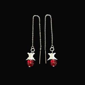 May include: A pair of dangle earrings with a unique design. Each earring features a small, white bone-like charm above a vibrant red, round bead. The beads are suspended from delicate silver chains.