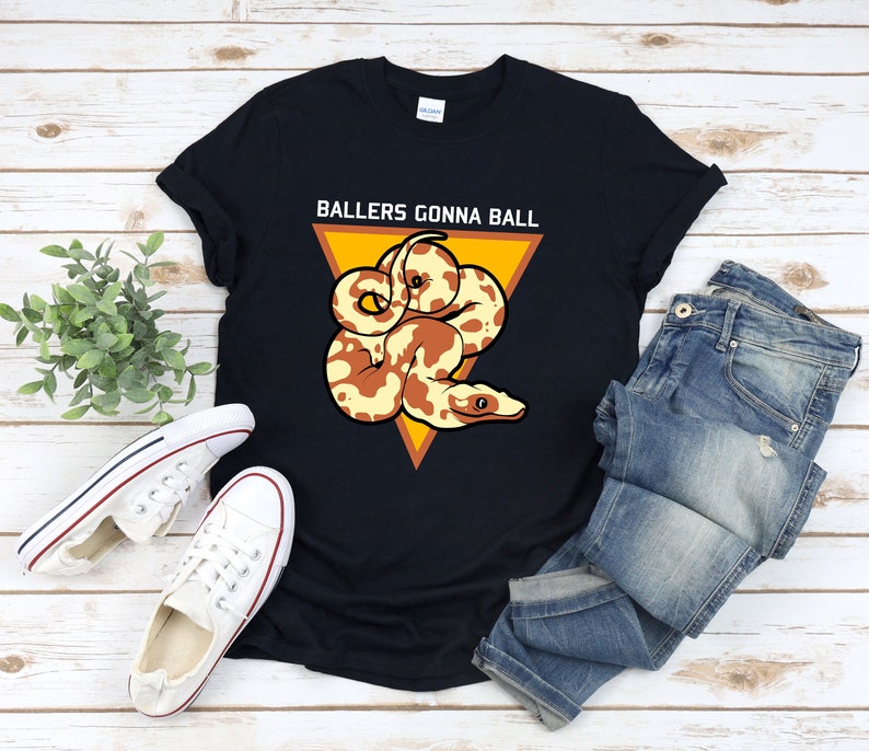 Op de afbeelding: Zwart T-shirt met een gele driehoek en een bruine en witte slang. De tekst "Ballers Gonna Ball" staat op het shirt gedrukt.