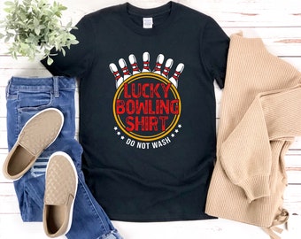 May include: Black t-shirt featuring a graphic of bowling pins and a bowling ball with the text "Lucky Bowling Shirt Do Not Wash" in red and yellow.
