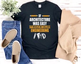 Può includere: Maglietta nera con una grafica bianca che dice "Se l'architettura fosse facile si chiamerebbe ingegneria" con un'illustrazione di una matita, un righello e un compasso.