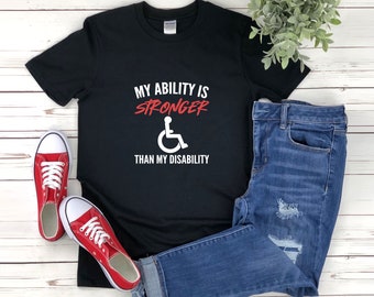 May include: Black t-shirt with the text "My ability is stronger than my disability" in white and red. A white wheelchair symbol is in the center of the shirt.