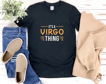 以下が含まれることがあります： 「It's a Virgo thing」というオレンジ色の文字が書かれた黒いTシャツ。文字の両側に乙女座の星座のシンボルがあります。