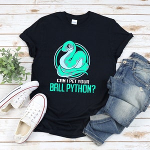 Peut inclure: T-shirt noir avec un serpent de dessin animé vert et le texte "Puis-je caresser ton python royal ?"