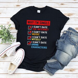 以下が含まれることがあります： 「WHY I'M SINGLE」の文字と、「I can't date the internet」や「I can't date anime characters」などの理由が書かれた黒いTシャツ。青いジーンズと白いスニーカーと組み合わせています。