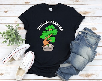 May include: Black t-shirt with a Bonsai Master graphic. The design features a stylized bonsai tree in a pot, with green leaves, a brown trunk, and the text "BONSAI MASTER" in white. The shirt is paired with blue jeans and white sneakers.
