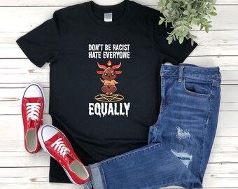 May include: Black t-shirt with the text "Don't be racist, hate everyone equally." The shirt features a cartoon illustration of a goat-like creature in a meditative pose, with a pentagram below. Red sneakers and blue jeans are also in the image.