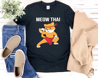 May include: Black t-shirt with a cartoon illustration of a cat in a red Muay Thai fighting outfit. The text "MEOW THAI" is printed in white above the cat.