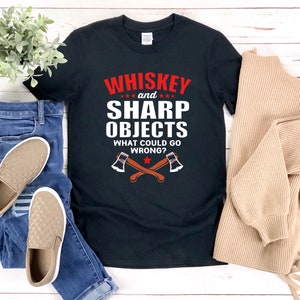 Puede incluir: Camiseta negra con texto blanco que dice "Whiskey and Sharp Objects What Could Go Wrong?" con una estrella roja y dos hachas cruzadas.