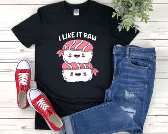 May include: Black t-shirt featuring a graphic of two sushi rolls with faces and the text "I like it raw". The shirt is paired with blue jeans and red trainers.