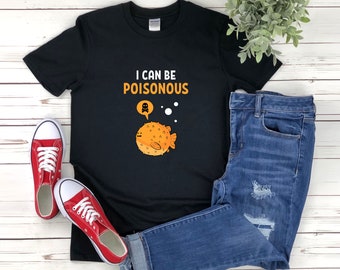Puede incluir: Camiseta negra con un gráfico de un pez globo y el texto "Puedo ser venenoso". La camiseta se combina con jeans azules y zapatillas rojas.