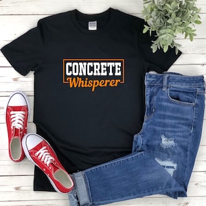 May include: Black t-shirt with the text "CONCRETE Whisperer" in a white rectangle with an orange outline.