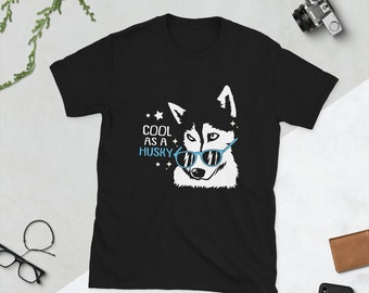 May include: Black t-shirt featuring a white husky dog wearing blue sunglasses. The text "COOL AS A HUSKY" is printed on the shirt.