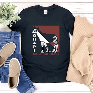 Può includere: T-shirt nera con un'illustrazione di okapi bianca e nera e il testo "OKAPI MAKES ME HAPPY".