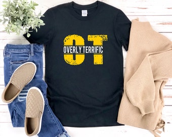 Op de afbeelding: Zwart T-shirt met een gele afbeelding die "OT" zegt voor "Overly Terrific".