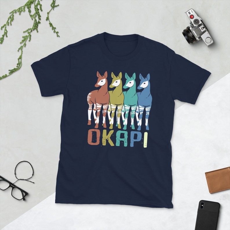 May include: A navy blue t-shirt with a retro-style graphic of four okapi, each a different color. The text "OKAPI" is printed below the animals.
