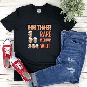 May include: Black t-shirt with a white graphic that says "BBQ Timer" and has beer mugs representing "Rare", "Medium", and "Well".