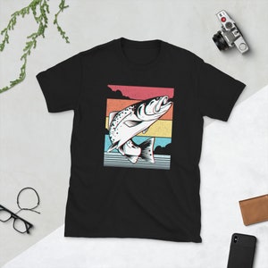 以下が含まれることがあります： 水から飛び出す魚のレトロなグラフィックがプリントされた黒いTシャツ。魚は白で黒いアウトラインがあり、カラフルなストライプの背景に配置されています。