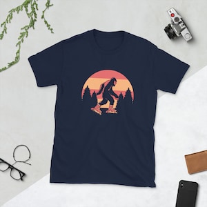 May include: A navy blue t-shirt with a graphic of a Bigfoot wearing roller skates in front of a sunset with trees.