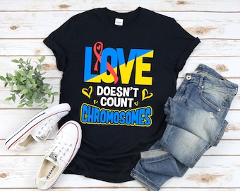 May include: Black t-shirt with a yellow and blue design that says "LOVE DOESN'T COUNT CHROMOSOMES". A red ribbon is incorporated into the design.