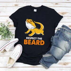 Op de afbeelding: Een zwart T-shirt met een cartoon afbeelding van een baardagame en de tekst "Respect the Beard" in oranje.