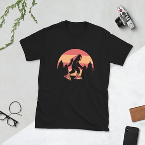 May include: Black t-shirt with a graphic of a Bigfoot wearing roller skates in front of a sunset.