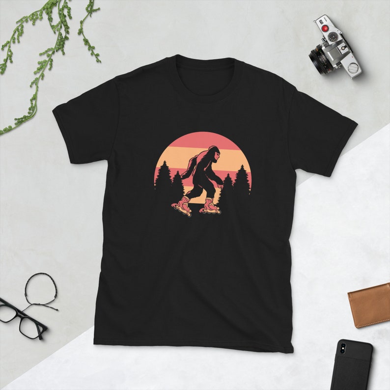 May include: Black t-shirt with a graphic of a Bigfoot wearing roller skates in front of a sunset.