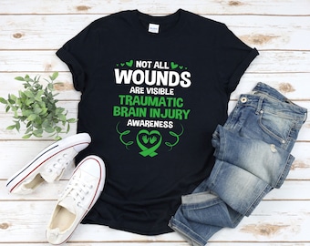 Op de afbeelding: Zwart T-shirt met een groen lint en de tekst "Niet alle wonden zijn zichtbaar. Traumatisch hersenletsel - Bewustzijn."