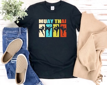 May include: Black t-shirt with a retro-style graphic of four people practicing Muay Thai. The text "MUAY THAI" is printed in colorful letters above the graphic.