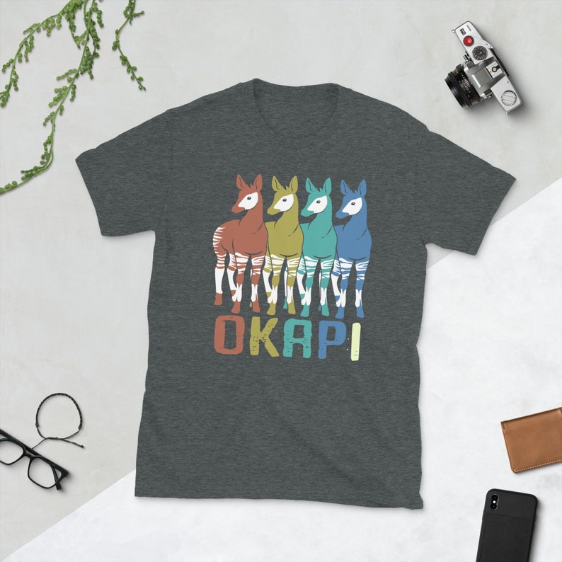 May include: A dark heather grey t-shirt with a retro-style graphic of four okapi, each in a different color: red, green, blue, and light blue. The word "OKAPI" is printed below the okapi in a vintage font.