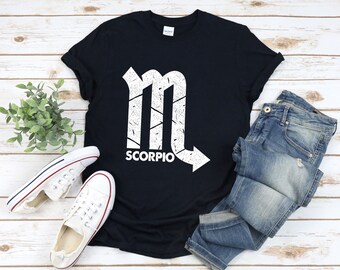 May include: A black t-shirt with a white distressed graphic of the Scorpio zodiac sign and the word "SCORPIO" printed below it.