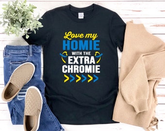 Puede incluir: Camiseta negra con el texto "Love my homie with the extra chromie" en letras amarillas y azules. El texto está rodeado de flechas amarillas y azules.