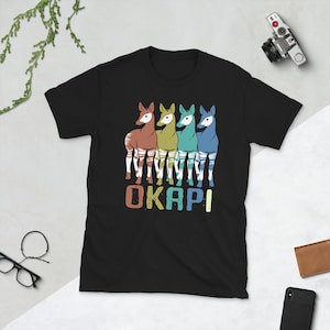 May include: Black t-shirt with a retro-style graphic of four okapi, each in a different color, with the word "OKAPI" printed below them.