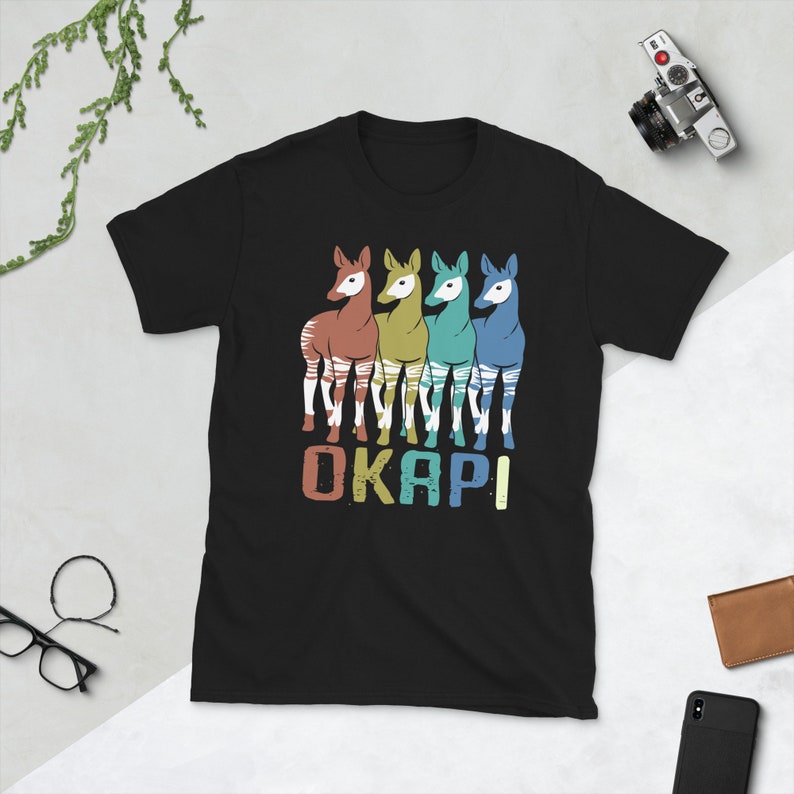 May include: Black t-shirt with a retro-style graphic of four okapi, each in a different color, with the word "OKAPI" printed below them.