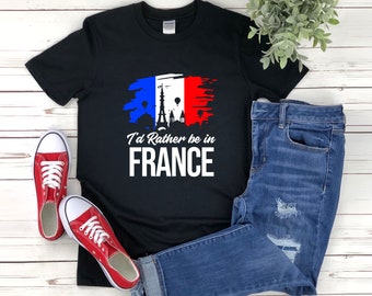 Puede incluir: Camiseta negra con un gráfico blanco de una bandera francesa estilizada con la Torre Eiffel y globos aerostáticos. El texto "I'd Rather be in FRANCE" está debajo del gráfico.