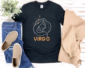 以下が含まれることがあります： 黒いTシャツに、女性の顔の白いアウトラインとオレンジ色の「おとめ座」の文字が描かれています。女性の顔は星の星座に囲まれています。
