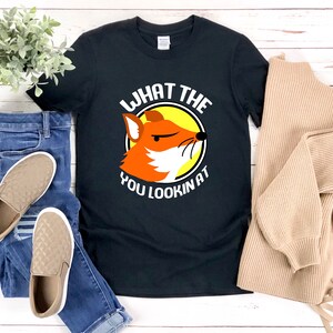 K&ouml;nnte beinhalten: Schwarzes T-Shirt mit einem Grafikdruck eines Fuchses mit dem Text "What the you lookin at" in Wei&szlig;.