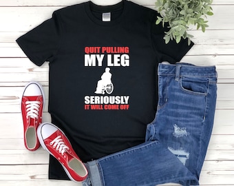 May include: Black t-shirt with white text that reads "Quit Pulling My Leg Seriously It Will Come Off". The text is in red. A white silhouette of a person in a wheelchair is above the text.