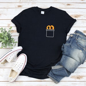 Pode incluir: Uma camiseta preta com um bolso na frente. O bolso tem um contorno branco e um par de pretzels dentro.