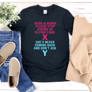 May include: Black t-shirt with a humorous message about algebra. The text reads "Dear Algebra, Please Stop Asking Us To Find Your X. She's Never Coming Back And Don't Ask Y." The letters X and Y are in pink and blue.