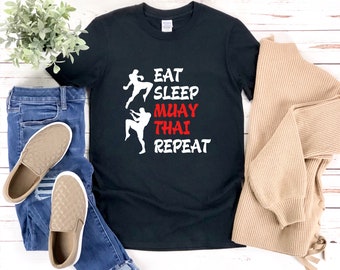 May include: Black t-shirt with white text that reads "Eat Sleep Muay Thai Repeat" and two white silhouettes of people doing a Muay Thai kick.