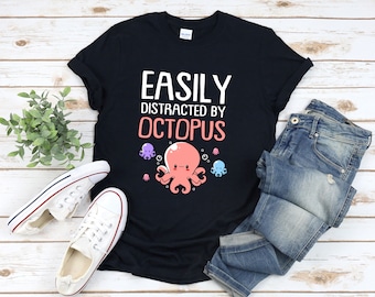 May include: Black t-shirt with white text that reads "Easily Distracted by Octopus". A pink octopus with a cute face is pictured below the text.