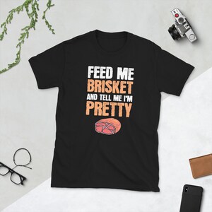 May include: Black t-shirt with white text that reads "Feed me brisket and tell me I'm pretty". A cartoon image of a slice of brisket is below the text.