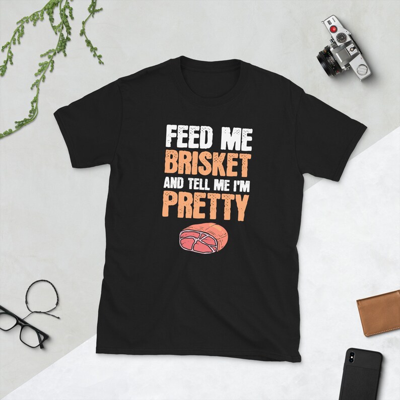 May include: Black t-shirt with white text that reads "Feed me brisket and tell me I'm pretty". A cartoon image of a slice of brisket is below the text.